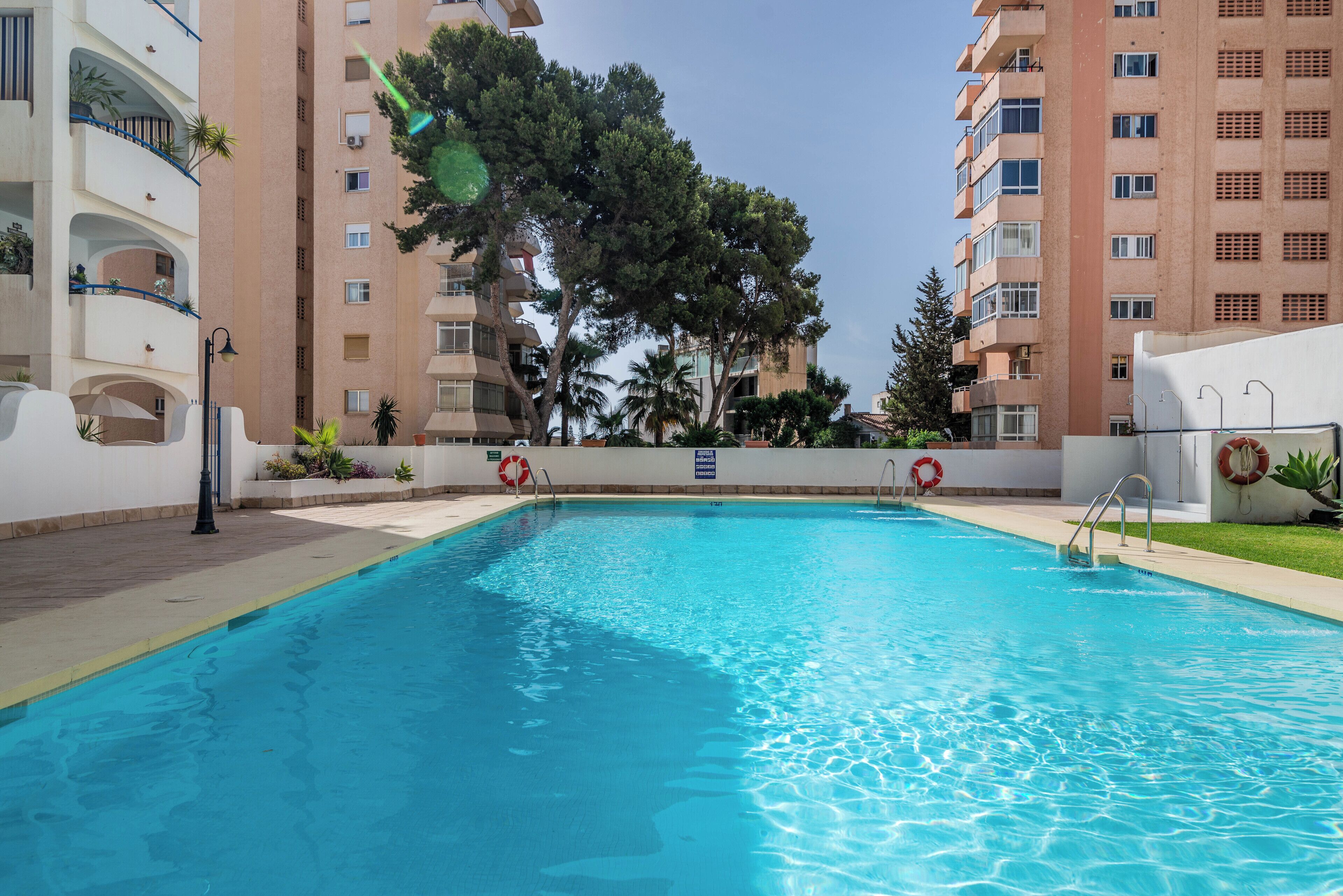 Ein Swimmingpool mit klarem, blauem Wasser, umgeben von einem weißen Gebäude mit Balkonen und Bäumen.