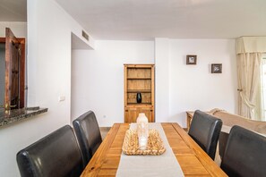 A dining area with a wooden table, black chairs, a woven placemat, and a wooden cabinet with a vase. - LXR Marysol II 2-Bedroom. Apt (Benalmádena)