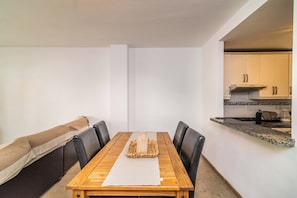 Ein Essbereich mit einem Holztisch, schwarzen Stühlen, einer gewebten Tischmatte und einer Bank mit cremefarbenem Kissen.
