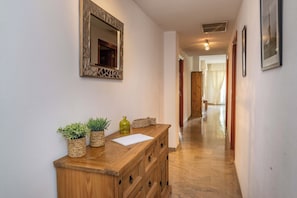 A hallway with a wooden cabinet, potted plants, a mirror, and framed pictures on the wall. - LXR Marysol II 2-Bedroom. Apt (Benalmádena)