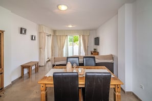 A dining area with a wooden table, black chairs, a sofa, and a television on the wall. - LXR Marysol II 2-Bedroom. Apt (Benalmádena)