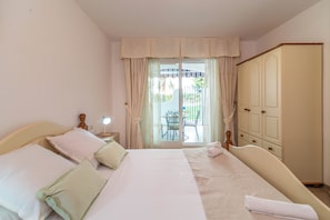A bedroom with a bed, a nightstand, a wardrobe, and a view of an outdoor patio. - LXR Marysol II 2-Bedroom. Apt (Benalmádena)