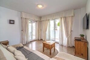 Ein Wohnzimmer mit einer Couch, einem kleinen Holztisch, einem Schrank und einem an der Wand befestigten Fernseher.