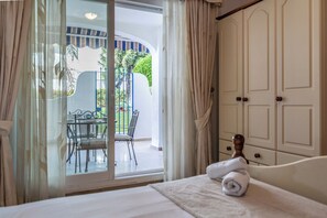A hotel room with a bed, a window with curtains, a view of an outdoor patio with a table and chairs, and a wardrobe. - LXR Marysol II 2-Bedroom. Apt (Benalmádena)