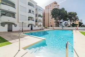A swimming pool with a clear blue water, surrounded by a white building with balconies and a tree. - LXR Marysol II 2-Bedroom. Apt (Benalmádena)