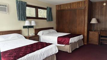 Habitación de hotel con dos camas, un armario, un escritorio y una lámpara.