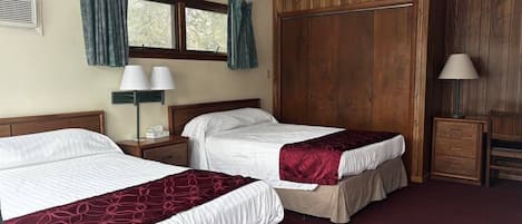 Una camera d'albergo con due letti, un armadio, una scrivania e una lampada.