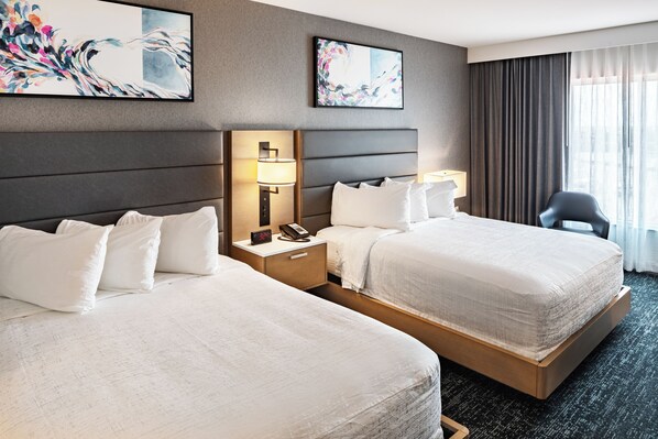 A hotel room with two beds, a nightstand with a lamp and phone, and artwork on the walls.