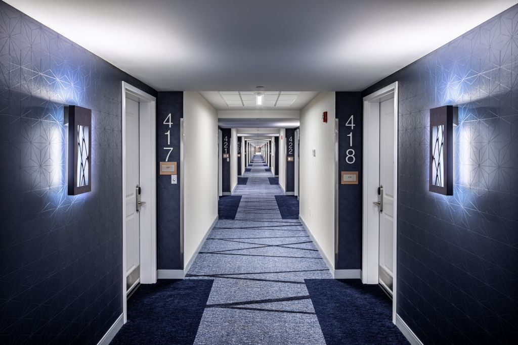 Corredor de hotel com portas numeradas 417 e 418, carpetes com padrão geométrico e paredes com design texturizado.