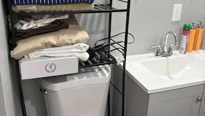 Une salle de bain équipée de toilettes, d’un lavabo et d’étagères où sont rangées les serviettes et les articles de toilette.