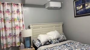 Une chambre à coucher avec un lit, une table de chevet, une lampe, un climatiseur et un tableau au mur.