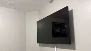Une chambre moderne avec un téléviseur à écran plat fixé au mur blanc, un luminaire au plafond et un tableau encadré.