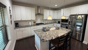 Una cocina moderna con armarios blancos, una isla de granito, electrodomésticos de acero inoxidable e iluminación colgante.
