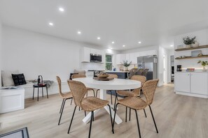 A modern kitchen with white cabinetry, a built-in oven, and a dining area with wicker chairs and a round table. - Stunning Lakefront Haven with Private Dock and Hot Tub (Blakeslee)