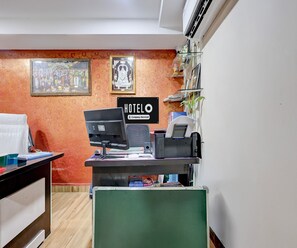 A hotel reception desk with a computer, phone, and a sign indicating it's a company-serviced hotel. - Deluxe Hotel O Satyam Junction (Visakhapatnam)