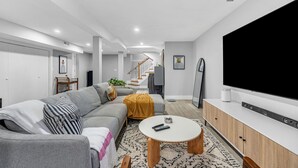 A modern living room with a grey sofa, a coffee table, a flat-screen TV, and a staircase in the background. - Modern 3-Bed, 2-Bath with AC in Everett Near Downtown, Airport, City & Encore (Everett)