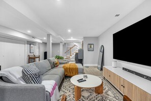 A modern living room with a grey sofa, a coffee table, a flat-screen TV, and a staircase in the background. - Modern 3-Bed, 2-Bath with AC in Everett Near Downtown, Airport, City & Encore (Everett)