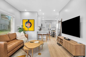 A modern living room with a sofa, coffee table, TV, and kitchen area. - Modern 3-Bed, 2-Bath with AC in Everett Near Downtown, Airport, City & Encore (Everett)
