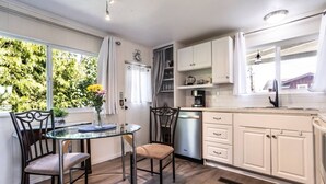 A modern kitchen with a dining area, white cabinets, a dishwasher, and a window with a view of greenery.