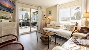 A living room with a sofa, a coffee table, a TV, and a view of the outside.