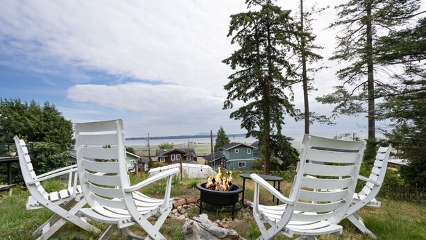 Two white Adirondack chairs facing a fire pit with a view of houses and trees.