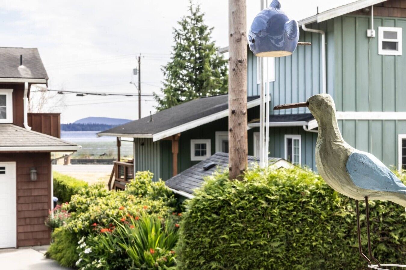 Zona residencial con una escultura de pájaro, una casa con garaje y vista al agua.