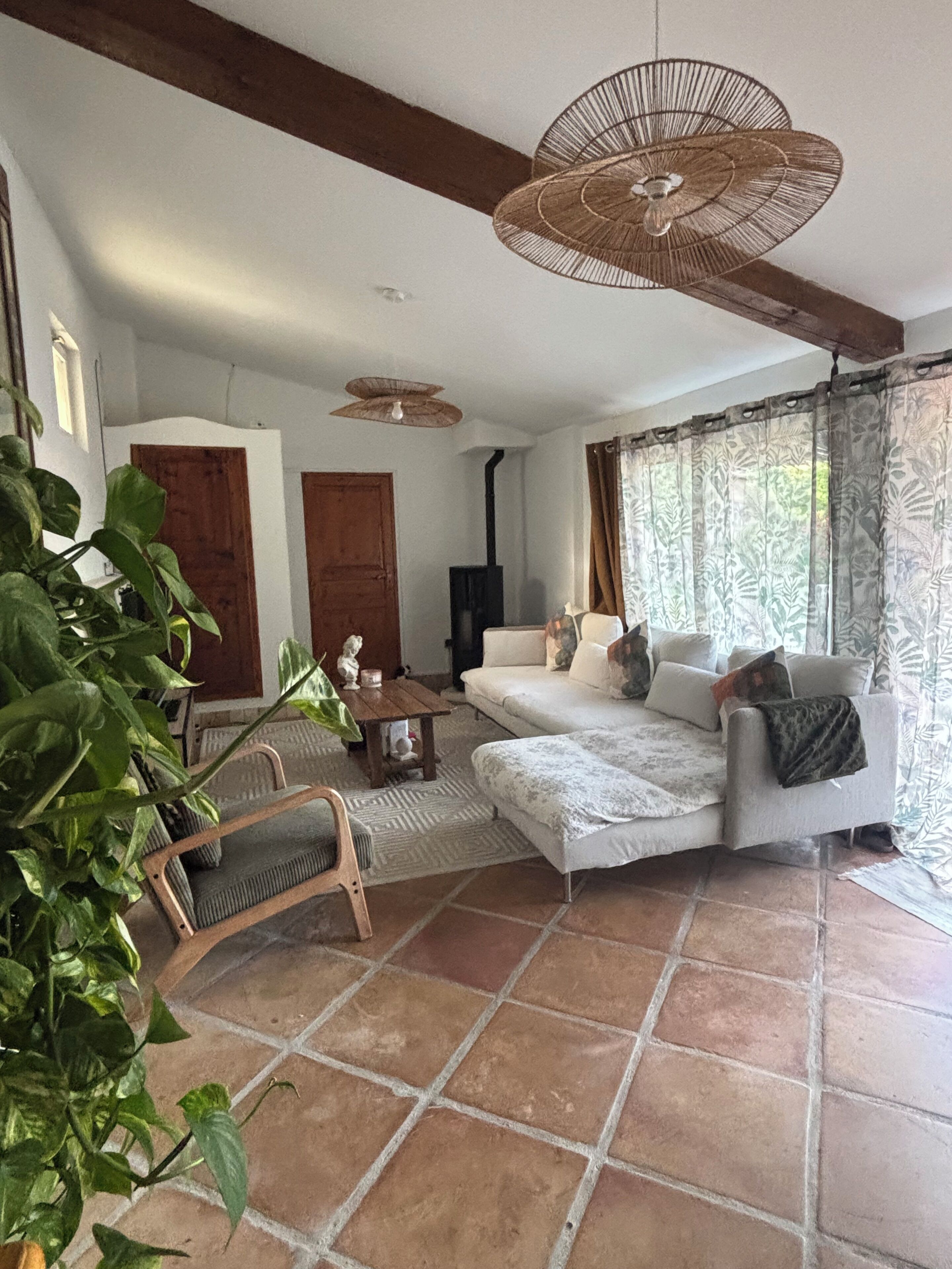 A living room with a sofa, a wooden coffee table, a hanging light fixture, and a large window with curtains.