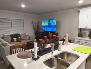 A modern kitchen with a central island, a dining area with a sofa, and a TV in the background. - Beautiful Palm Coast Escape Near Beaches (Palm Coast)