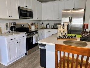 A modern kitchen with white cabinetry, stainless steel appliances, and a central island with a 'welcome' sign. - Beautiful Palm Coast Escape Near Beaches (Palm Coast)