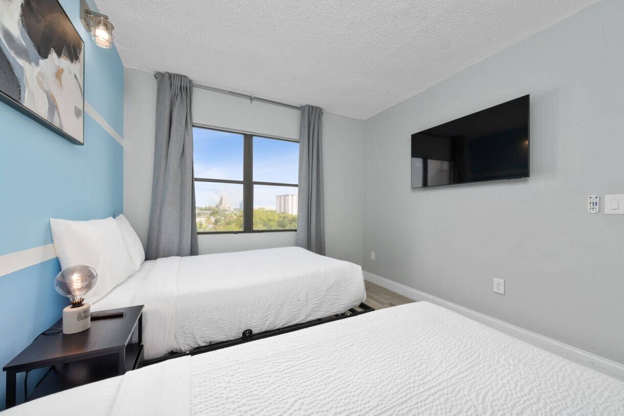 Quarto de hotel com duas camas, televisão, janela com cortinas e um quadro na parede.