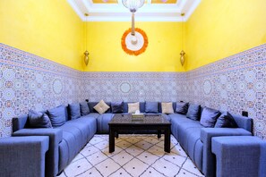Ein Zimmer mit blauem Sofa, einem gemusterten Teppich und einem Deckenventilator.