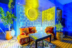 Ein Zimmer mit einem gemusterten Wand, einem Sofa mit Kissen, einem Tisch und zwei Blumentöpfen.