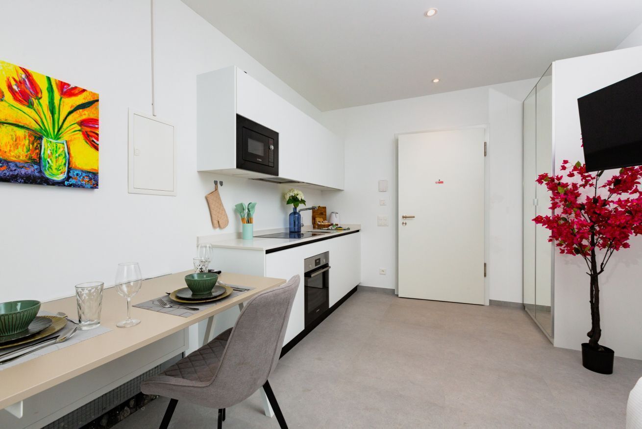 A modern kitchen with white cabinetry, a microwave, and a dining area with a table and chairs.