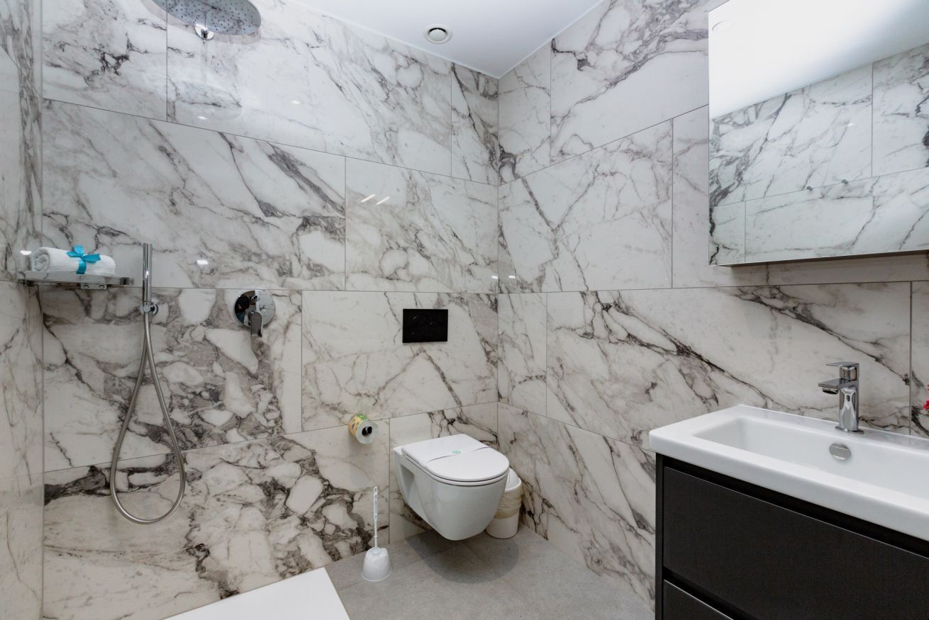 Een badkamer met marmeren wanden, een toilet, een douche en een wastafel.