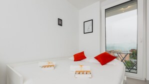 Ett modernt hotellrum med en stor säng, två röda kuddar, ett fönster med utsikt över staden och en liten inramad tavla på väggen.