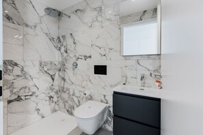 A bathroom with a marble wall, a shower, a toilet, and a sink with a mirror above. - {Suite 614} Gym, Business Room, Modern, Relax (Lugano)