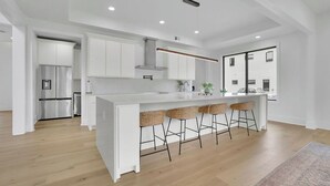 A modern kitchen with white cabinetry, a central island with bar stools, and a stainless steel refrigerator. - Luxury 4-bedroom home with 2 kitchens, hot tub, and gym: Group & Family Retreats (Marietta)