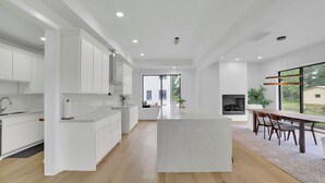 A modern kitchen with white cabinetry, a central island, and a dining area with a long table and chairs. - Luxury 4-bedroom home with 2 kitchens, hot tub, and gym: Group & Family Retreats (Marietta)