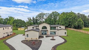 A modern residential building with a curved driveway, multiple entry points, and a well-maintained lawn. - Luxury 4-bedroom home with 2 kitchens, hot tub, and gym: Group & Family Retreats (Marietta)