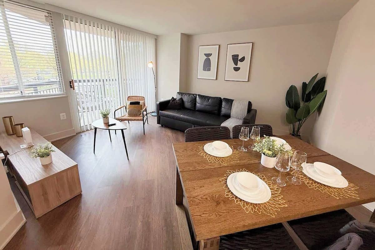Una sala moderna con comedor, un sofá de cuero negro y una mesa de comedor preparada para cuatro.