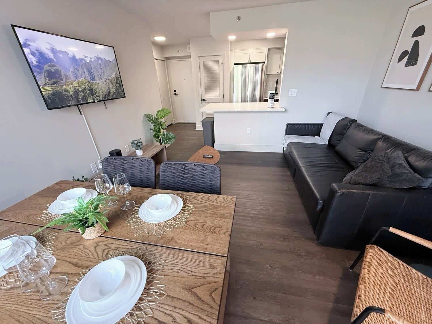 Een moderne woonkamer met een houten salontafel, een zwarte leren bank en een aan de muur bevestigde televisie.
