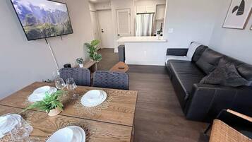 Een moderne woonkamer met een houten salontafel, een zwarte leren bank en een aan de muur bevestigde televisie.