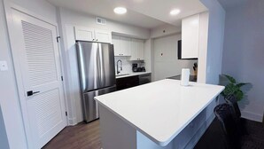 A modern kitchen with white cabinetry, a stainless steel refrigerator, a built-in oven, and a large white countertop.