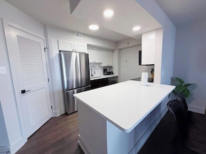 A modern kitchen with white cabinetry, a stainless steel refrigerator, a built-in oven, and a large white countertop. - Beautiful Apt in the Heart of Pentagon (Arlington)