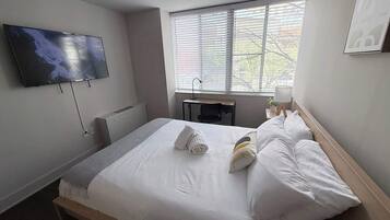 Een hotelkamer met een bed, een aan de muur bevestigde televisie, een bureau en een raam met jaloezieën.