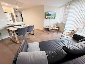 A modern living room with a sofa, a dining area with chairs, a kitchen with a refrigerator, and a TV mounted on the wall. - Beautiful Apt in the Heart of Pentagon (Arlington)