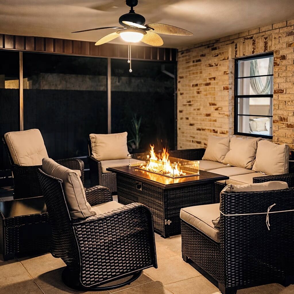 A cozy outdoor seating area with wicker furniture, a glass-top fire pit, and a ceiling fan.