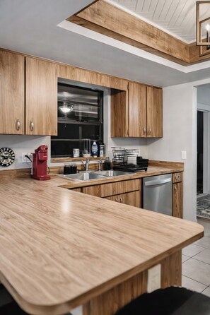 A modern kitchen with wooden cabinets, a stainless steel sink, and a red coffee maker. - 5BR Pool Home w/ Fire Pit . Sleeps 10 (Deltona)