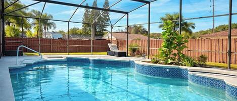 A swimming pool with a clear blue water, surrounded by a wooden fence, and a metal roof structure.