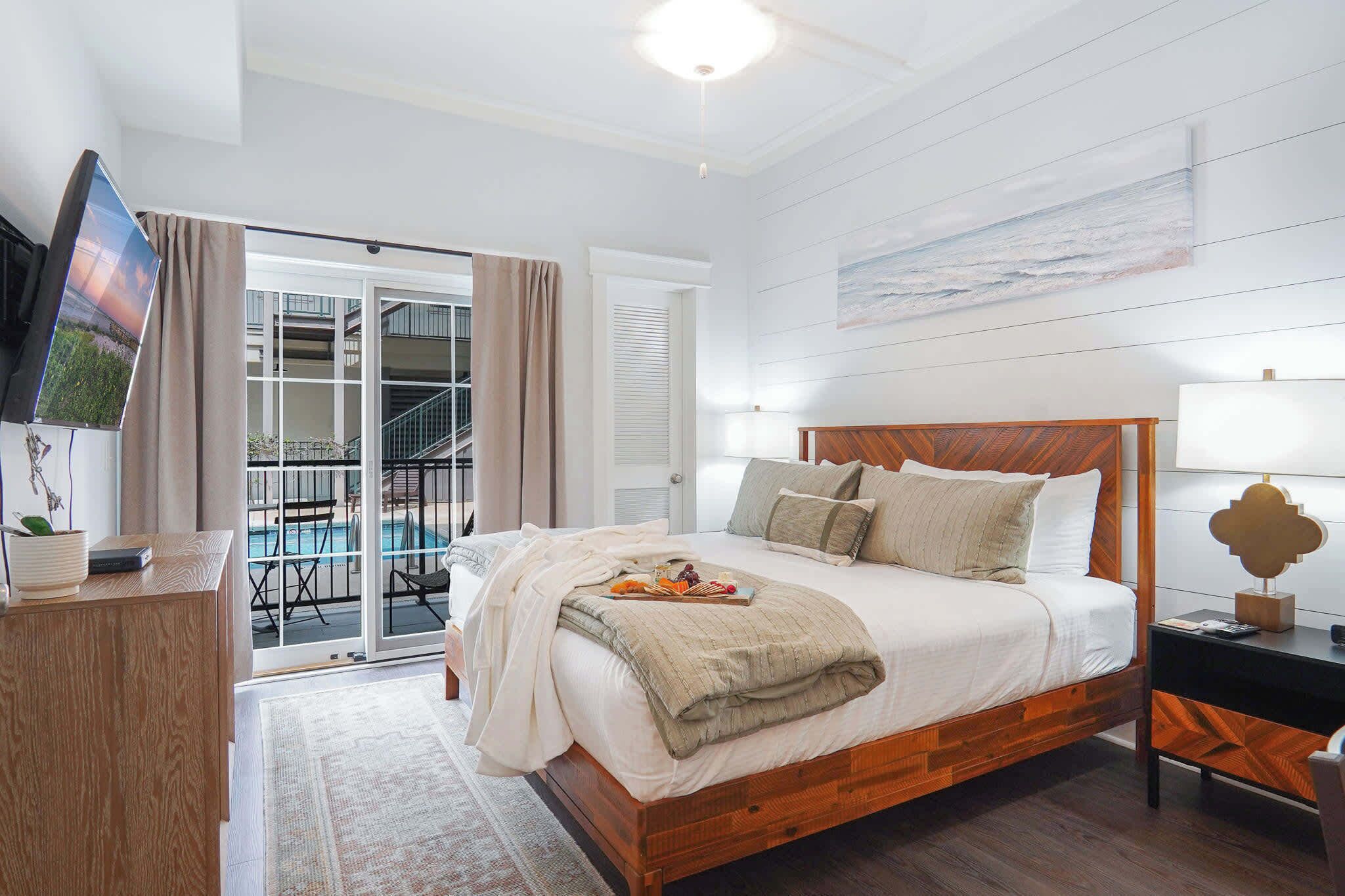A bedroom with a bed, bedside tables, a TV, and a view of a balcony.